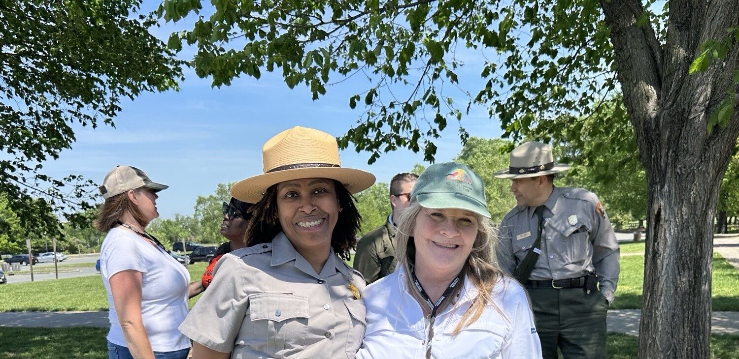 Superintendent and Executive Director stand next to each other in a park on a sunny day.